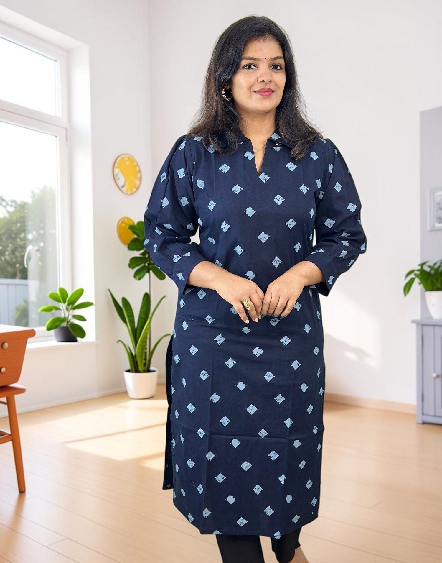A woman modeling a navy blue cotton kurta with a light blue geometric diamond pattern, standing in a bright, modern room with wooden floors and potted plants.