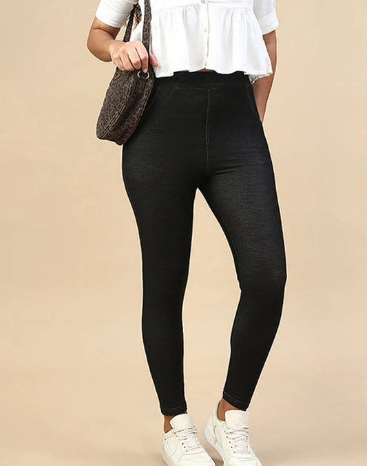 A model wearing black high-waisted skinny leggings, a white ruffled blouse, and white sneakers, holding a brown textured shoulder bag against a solid beige background.