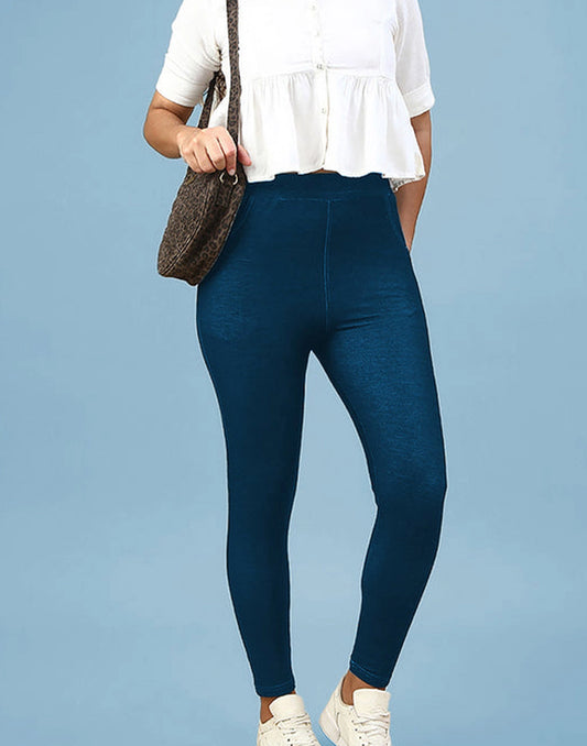 A model wearing dark blue high-waisted leggings, a white short-sleeve peplum blouse, and white sneakers, carrying a brown textured shoulder bag against a solid light blue background.