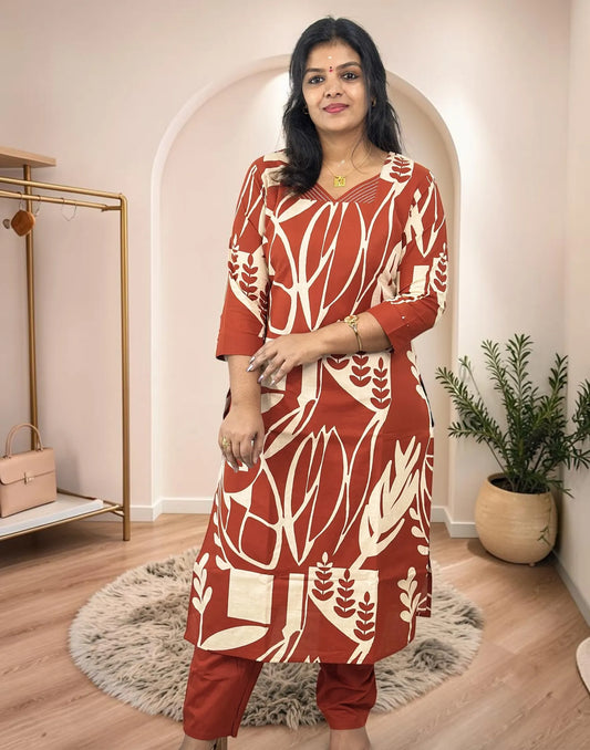 A woman modeling a rust-red and cream printed kurta with matching pants in a styled indoor boutique setting.