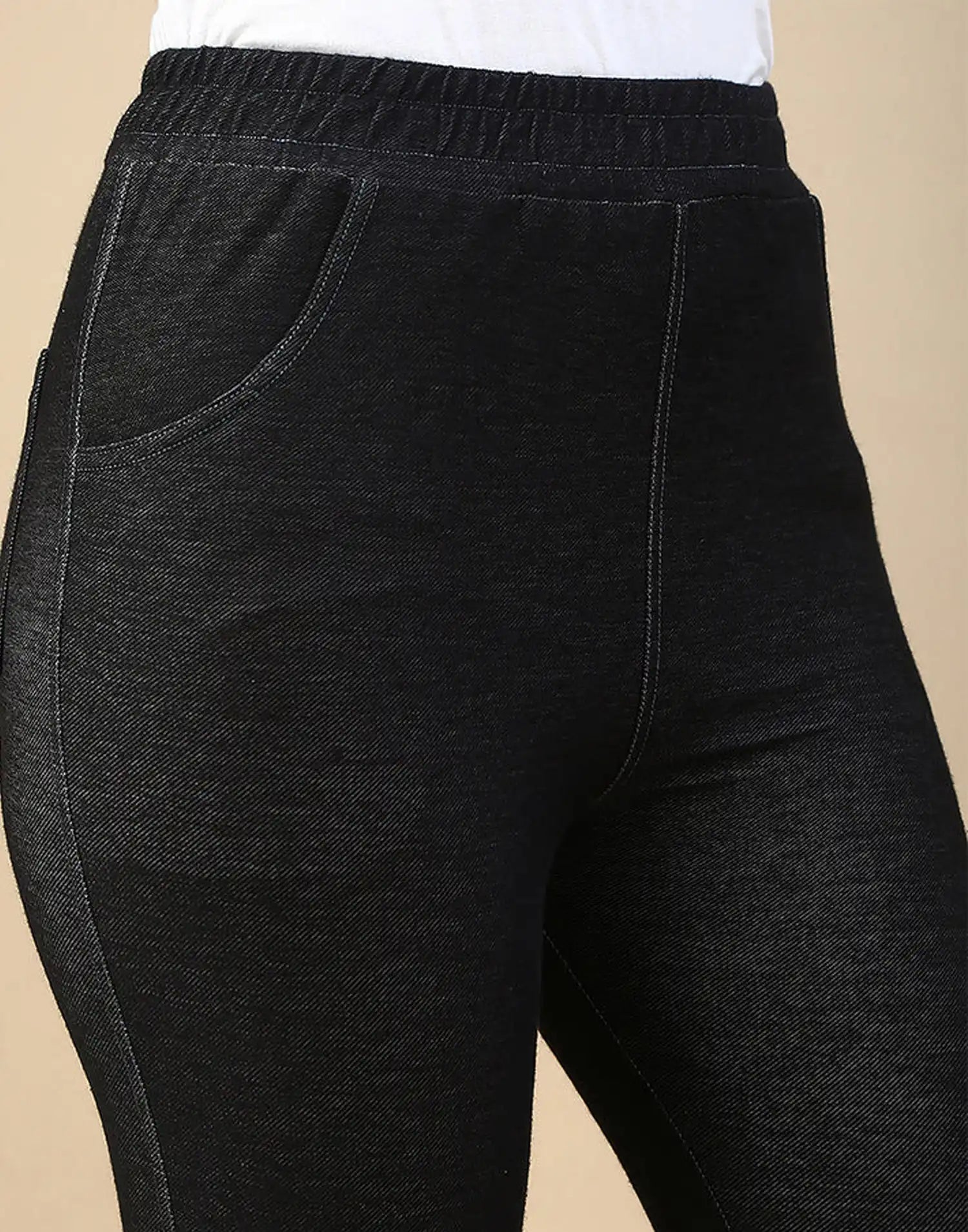 Close-up of a person wearing dark charcoal heathered jogger-style pants with an elastic waistband and side pockets, paired with a white top against a plain beige background.