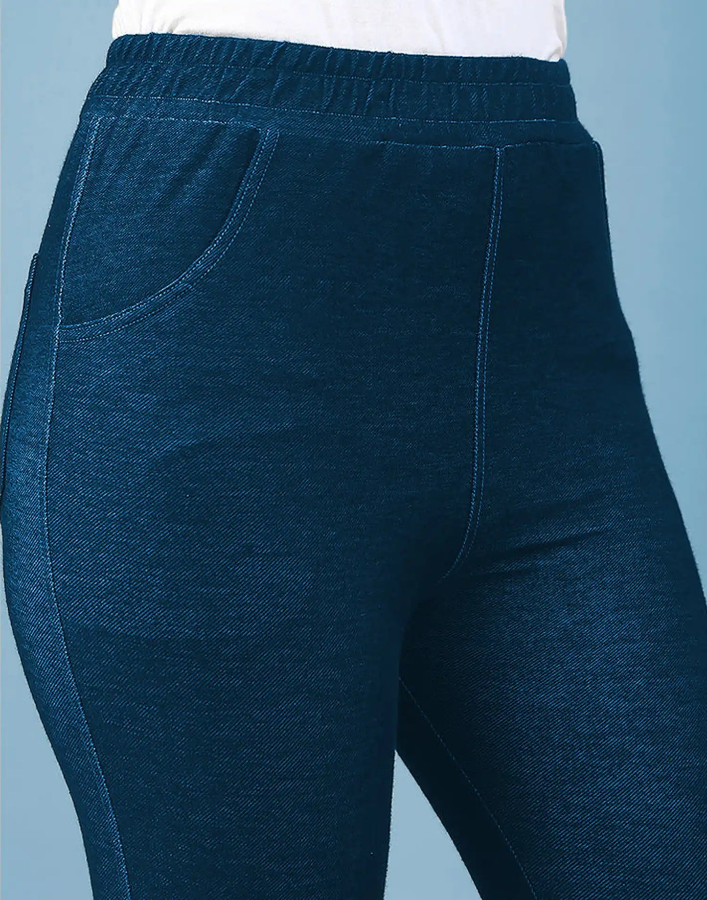 Close-up of a person wearing dark heather blue jogger-style pants with an elastic waistband and side pockets, against a light blue background.