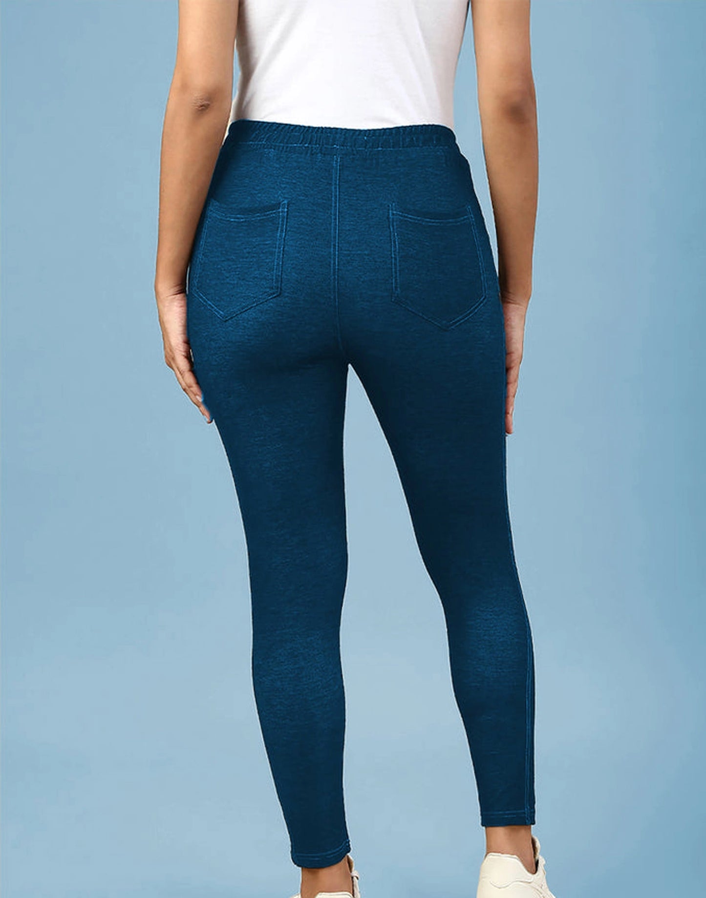 A person shown from the back wearing dark blue heathered leggings with a white top, standing against a light blue studio background.