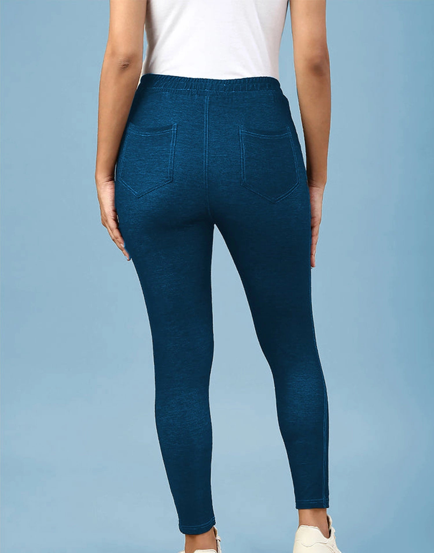 A person shown from the back wearing dark blue heathered leggings with a white top, standing against a light blue studio background.